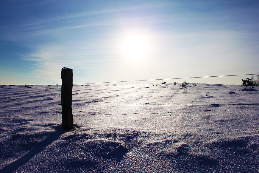 Lone wooden post in snowy landscape under bright sun