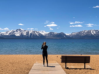 Woman Taking Photo of Snowy Mountains by Lake