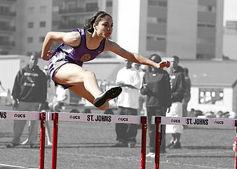 Female athlete jumping hurdles in purple uniform
