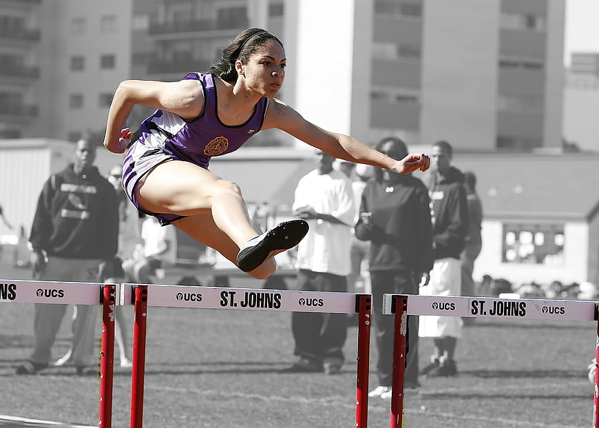 Female athlete jumping hurdles in purple uniform