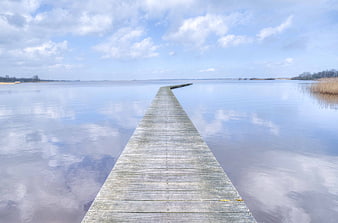 Wooden pier extending into calm lake with sky reflection