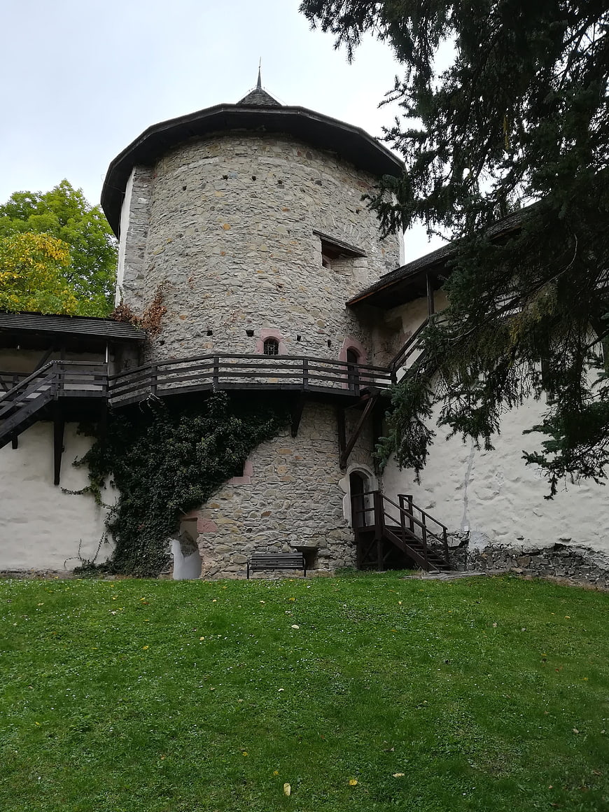 Historic stone castle tower with wooden walkway and green lawn