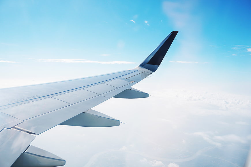Airplane Wing View Over Clouds and Blue Sky