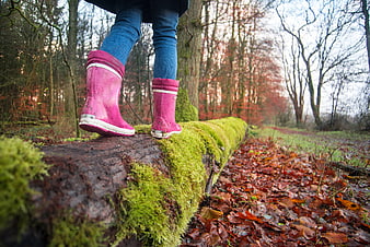 Child in pink rain boots walking on mossy log in autumn forest