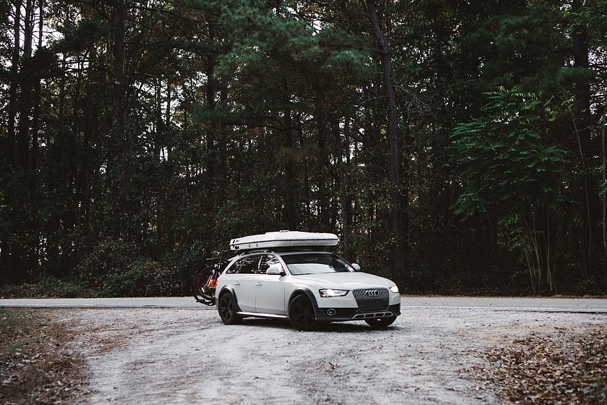White Audi Allroad with Roof Box and Bikes in Forest