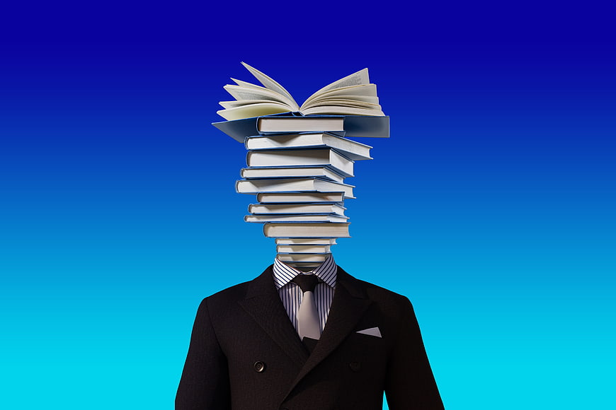Conceptual businessman with stack of books for head on blue background