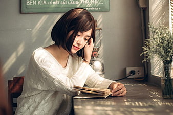 Young woman reading book in cozy cafe with natural window light