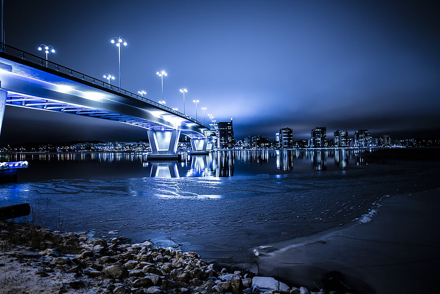 Illuminated bridge over frozen river with city skyline at night