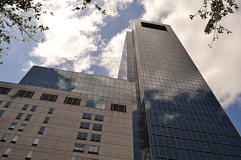 Low angle view of modern glass skyscraper and office building against cloudy blue sky