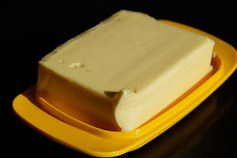Block of butter on yellow dish against black background