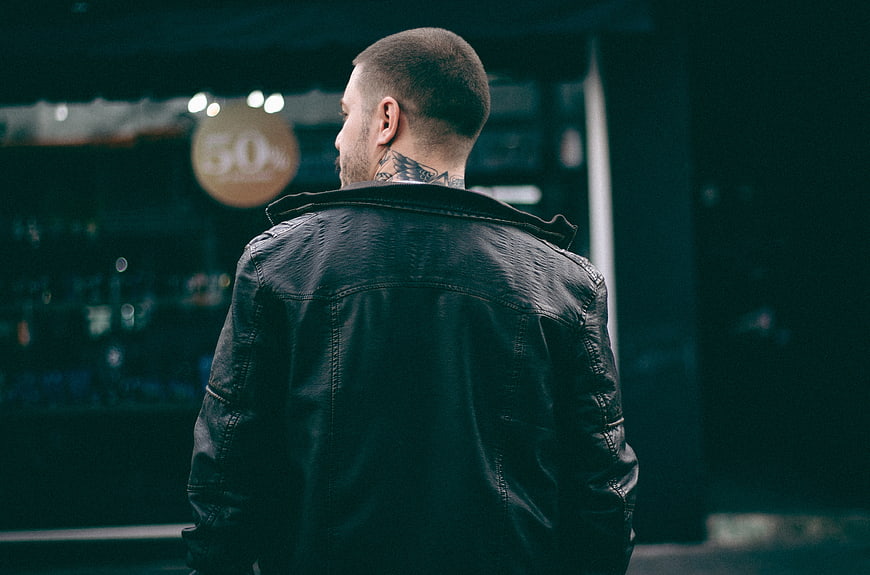 Man in Leather Jacket with Neck Tattoo Looking at Store Window