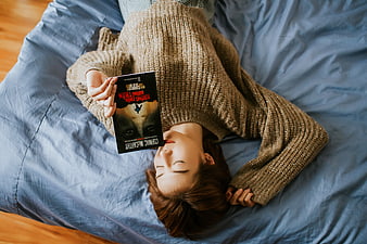 Woman sleeping on bed holding book overhead
