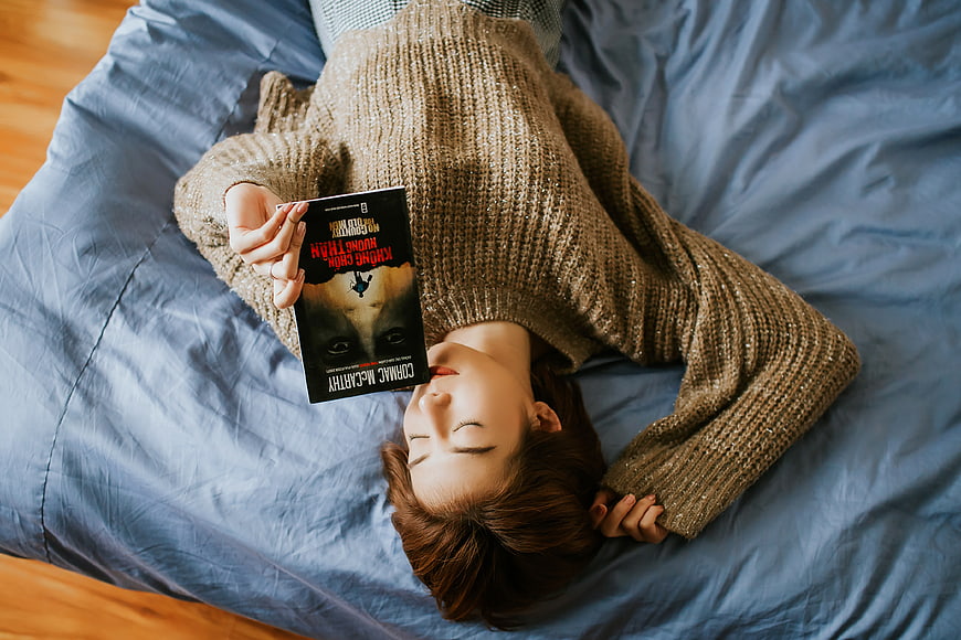 Woman sleeping on bed holding book overhead