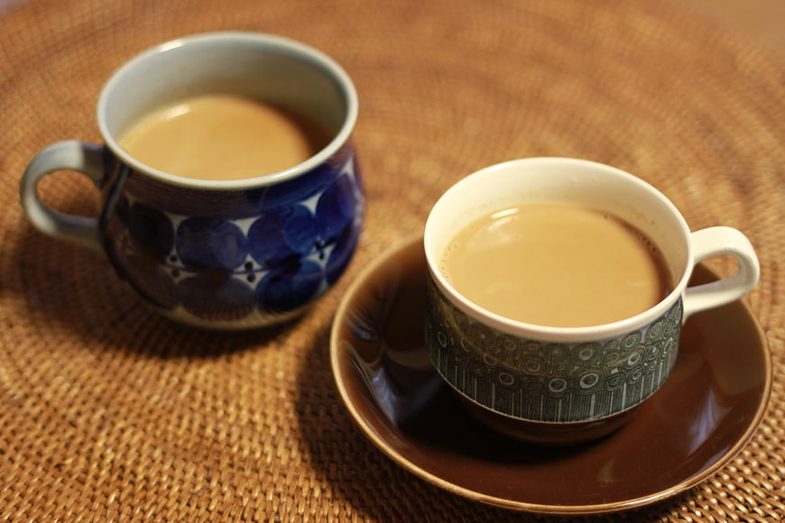 Two ceramic cups of milk tea on a woven rattan placemat