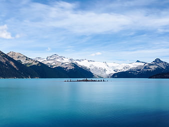 Serene turquoise alpine lake with snow-capped mountains and floating logs