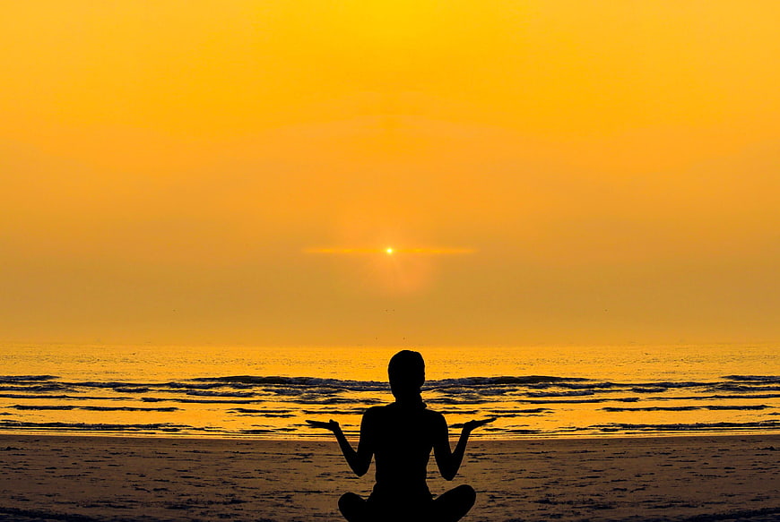 Silhouette of woman meditating in lotus position on beach at sunset