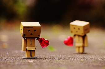 Two cardboard Danbo robots holding red hearts on a path
