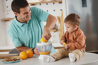 Father and son making fresh orange juice in kitchen