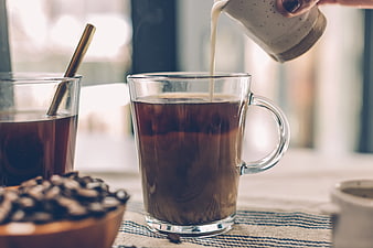 Pouring milk into hot coffee with beans