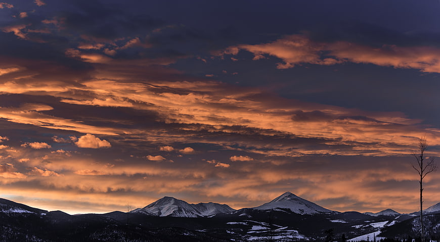 Dramatic sunset over snow-capped mountain peaks with orange clouds