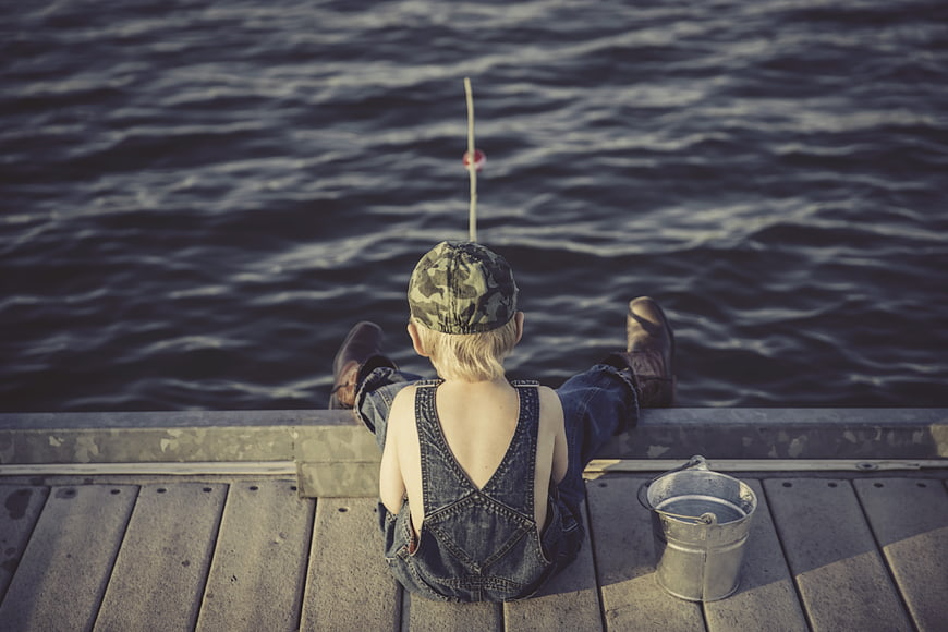 Child fishing on wooden dock with bucket