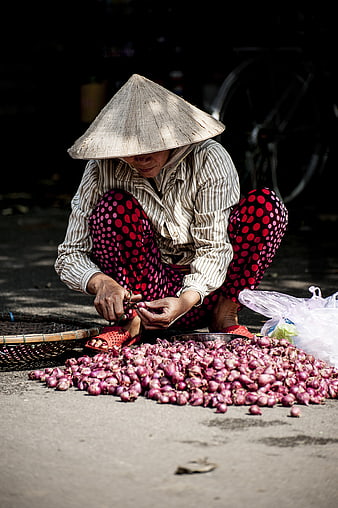 Vietnamese woman in conical hat sorting red onions