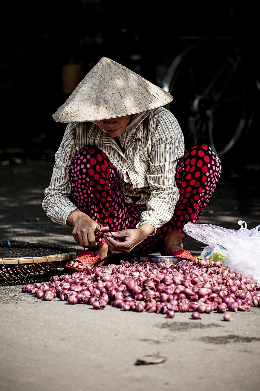 Vietnamese woman in conical hat sorting red onions