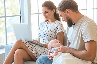Young Parents with Sleeping Baby and Laptop at Home