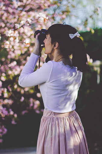 Woman photographer taking photo under cherry blossoms