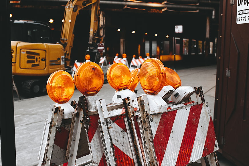 Construction barriers with orange lights and excavator background