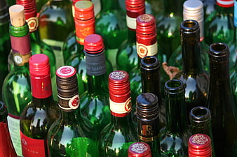 Close-up of assorted green glass wine bottles with colorful caps