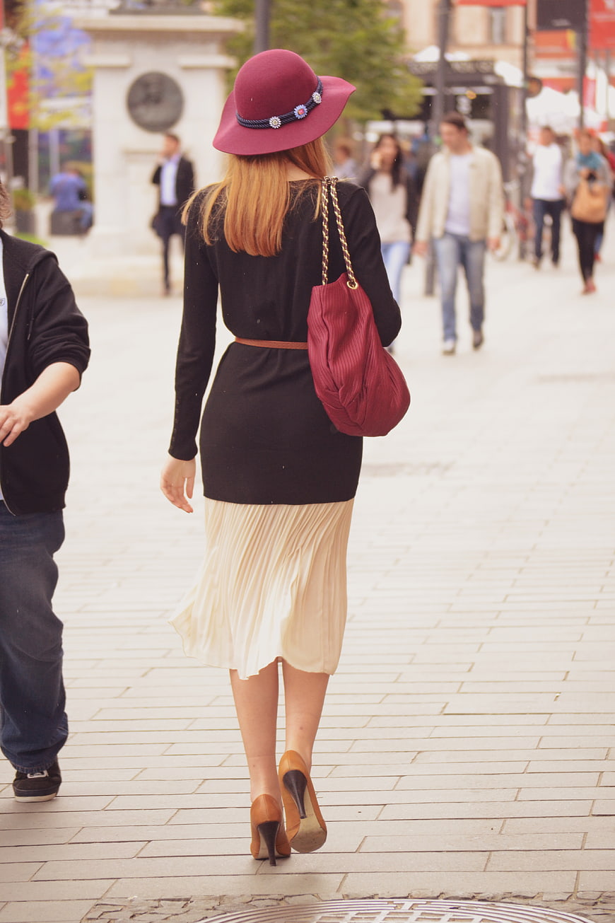 Stylish Woman Walking Away in Burgundy Hat and Pleated Skirt