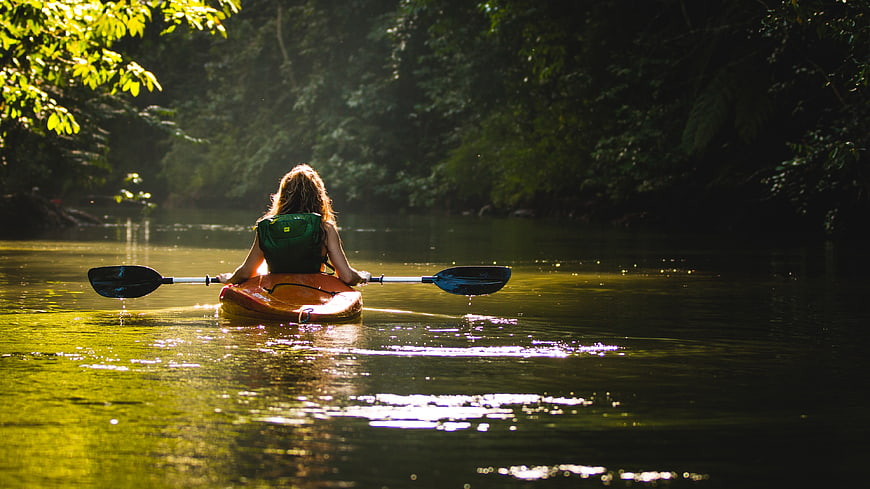 Woman Kayaking on Sunlit River in Forest