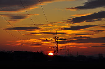 Silhouette of electricity pylons against a vibrant orange sunset sky