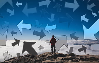 Man on mountain summit facing many directional arrows in sky