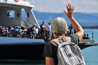 Senior woman waving goodbye to ferry passengers at a sunny lake port