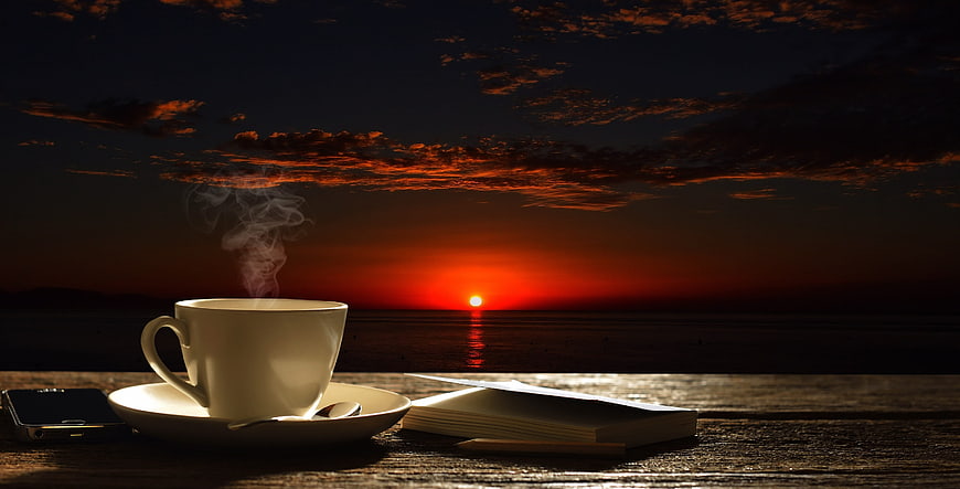 Steaming Coffee Cup on Wooden Table with Sunset Ocean View