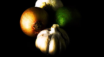 Dramatic still life of onion, garlic, and lime on black background