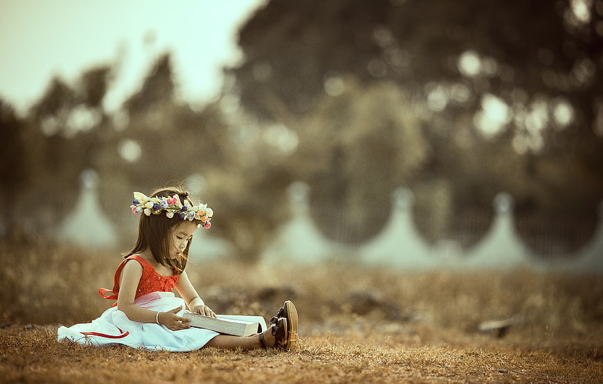 Little girl reading book in field with flower crown