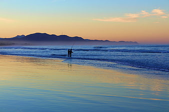 Silhouetted Fishermen on Beach at Sunset with Mountain Reflection