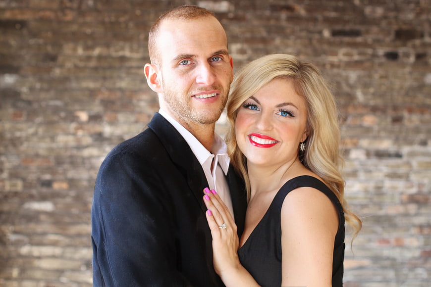 Happy engaged couple posing with ring against brick wall
