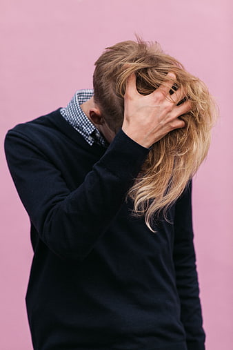 Man with blonde mullet hiding face in hand against pink background