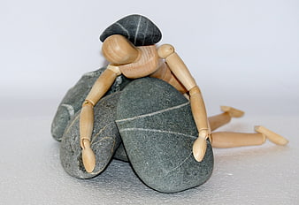 Wooden artist mannequin struggling under heavy grey stones