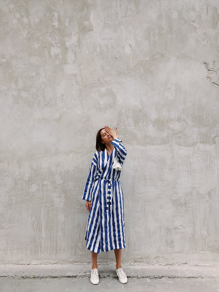 Woman in Blue Striped Dress Against Concrete Wall