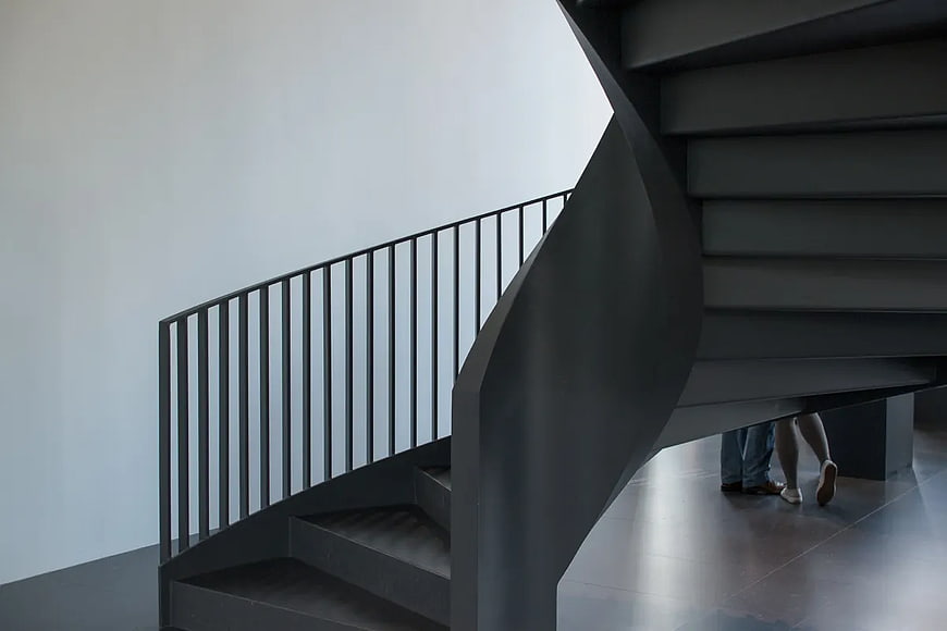 Modern black spiral staircase with people walking underneath