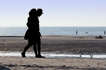 Silhouette of couple walking on sandy beach at sunset
