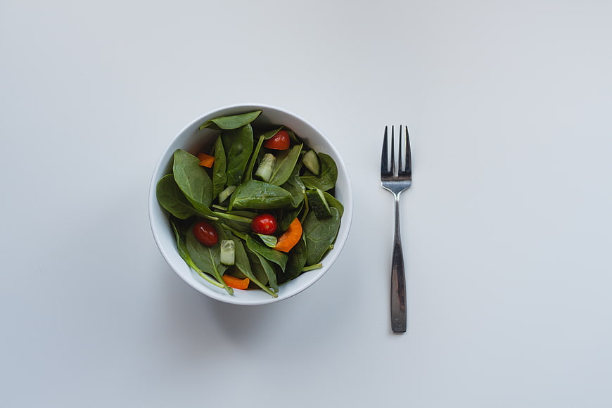 Top View of Fresh Green Salad Bowl with Fork on White Background
