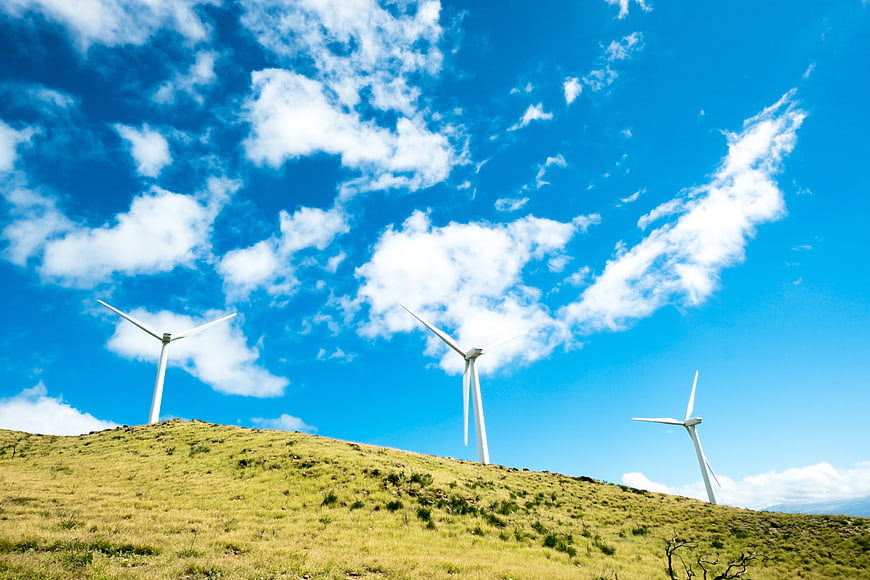 Wind turbines on grassy hill under blue sky