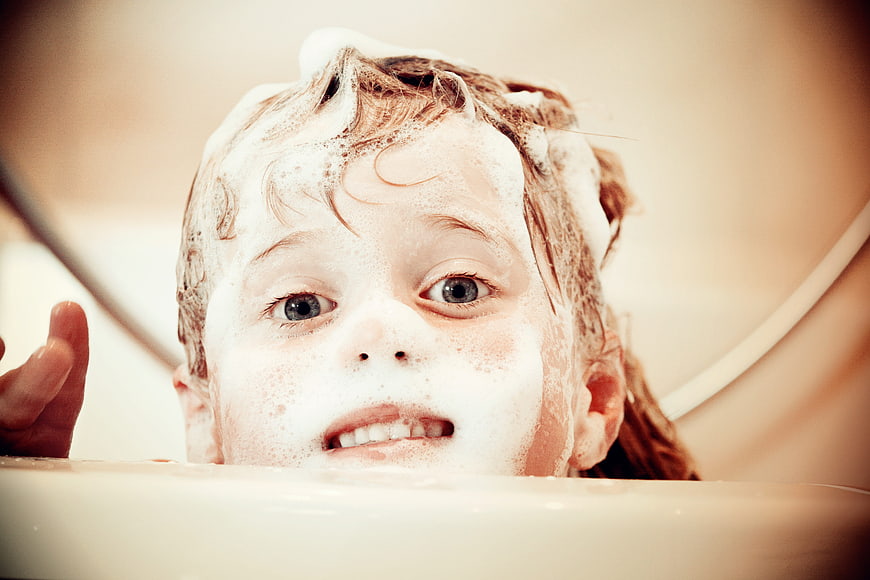 Close-up of a young girl with soapy hair in a bathtub