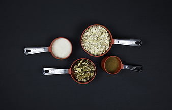 Red Measuring Cups With Oats, Nuts, And Spices On Black Background